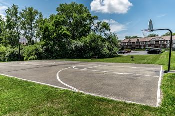 A tennis court surrounded by a fence and trees with apartment buildings in the background